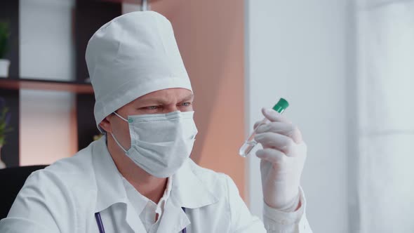 A male medic in a mask and gloves examines a test tube.