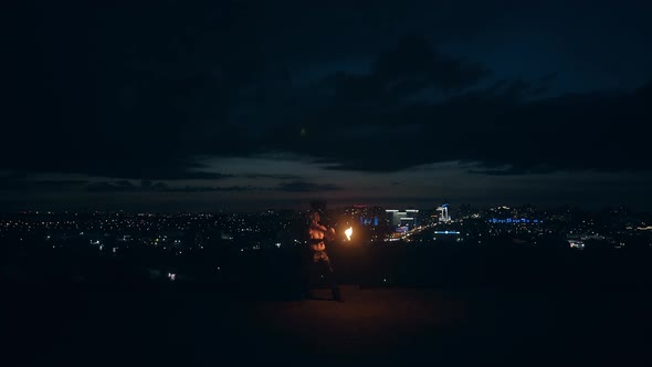 Young Blond Male Does Tricks with Fire Breaths Fire in the Middle of the Night with City Skyline in alt