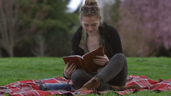 Young woman at park sitting on blanket looking at book