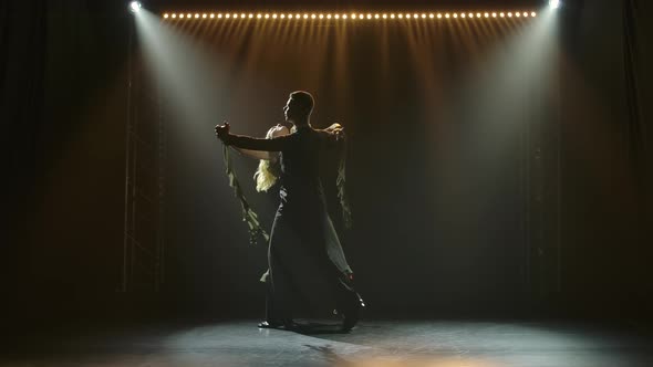 A Couple of Ballroom Dancers Are Spinning in a Waltz Against the Backdrop of Blue Lights. Silhouette alt