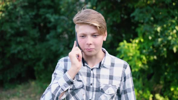 Young Caucasian Teenager Man in a Light Gray Checkered Shirt Speaks on the Phone alt