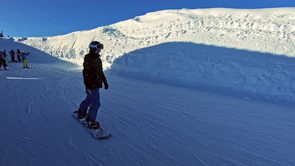 A teenage boy on a snowboard sliding by slowly. alt