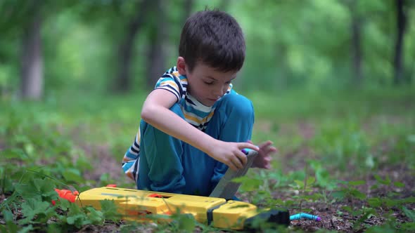 A Boy Loads a Clip with Cartridges From a Toy Machine Gun Outdoors
