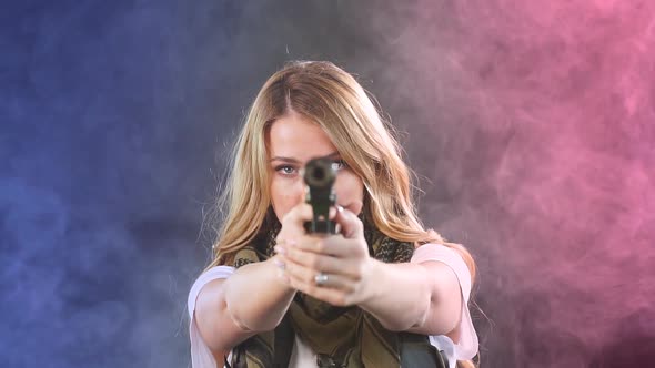 Armed Blonde Woman Shoots with Gun at a Target in the Darkness with Smoke Clouds alt
