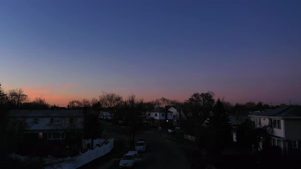 An aerial shot over a suburban neighborhood during sunrise. The camera dolly in & boom up towards th alt