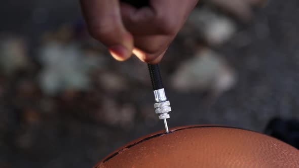 A young man pumping up his basketball on an outdoor street court. alt