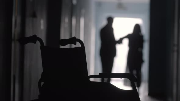 Silhouette of Man Supporting Limping Woman in Hospital Hallway