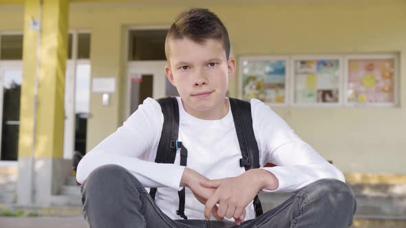 A Caucasian Teenage Boy Smiles at the Camera As He Sits in Front of School  Closeup