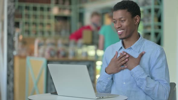 Cheerful African Man Doing Video Call on Laptop in Cafe alt