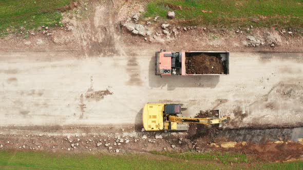 Aerial View of Excavator Loading a Dump Truck with Soil in the Green Field alt