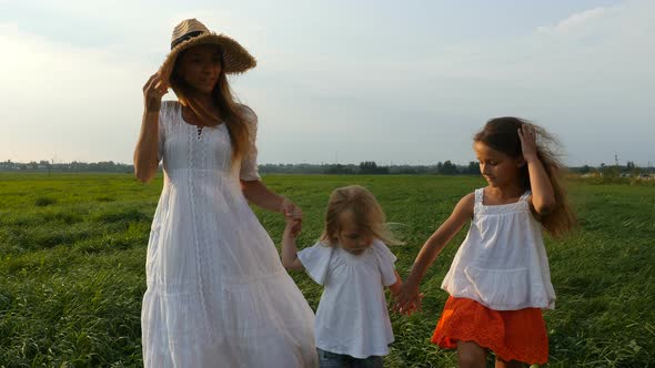 Happy Family, Mother and her Little Daughters Walk on the Green Grass, Summer Evening