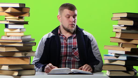 Man Sitting at His Desk Leafing Through a Textbook. Green Screen alt