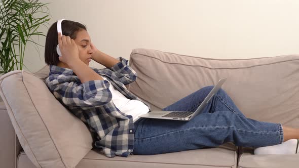 A Woman in Jeans with Headphones Using a Silver Laptop Lying on a Sofa