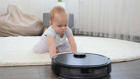 Cute Baby Boy Crawling on Floor and Looking on Robot Vacuum Cleaner alt