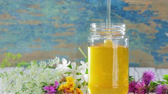 A Stream of Fresh Honey Flows Down in Glass Jar on the Rustic Background alt