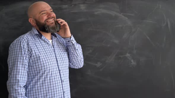 Adult Caucasian Man Talking on a Mobile Phone Standing Near a Chalkboard in a College or University alt