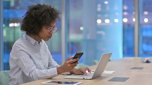 Hardworking African Businesswoman Using Smartphone and Laptop in Office  alt