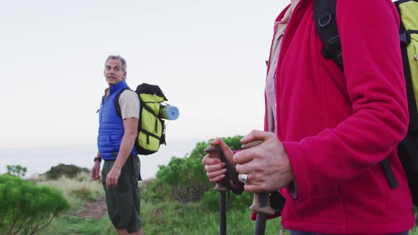 Senior hiker couple with backpacks and hiking poles looking at each other standing alt
