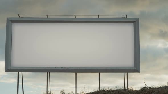 Blank White Billboard on the Background of the Sky with Moving Clouds in the Sunset Light alt
