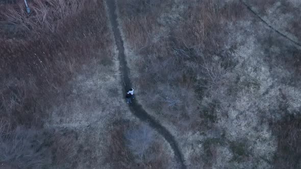 A top down view directly above two people walking on a dirt path in a park during a cloudy evening. alt