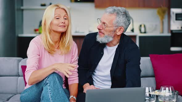 Adult Man and Woman are Sitting on a Cozy Sofa Choosing a Movie to Watch Together alt