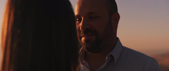 Close up of a young man looking at his girlfriend with love at sunset.  alt