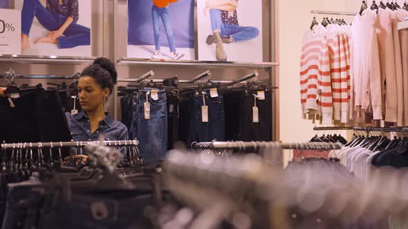 Female Customer Makes Purchases in Clothing Store Chooses Stylish Clothes Hanging on Rack Hangers alt