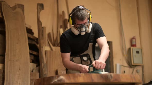Wood craftsman grinds a piece of wood for a table in a workshop alt
