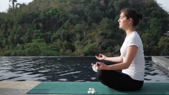 Young Woman Sits in a Lotus Position Near the Rooftop Pool alt