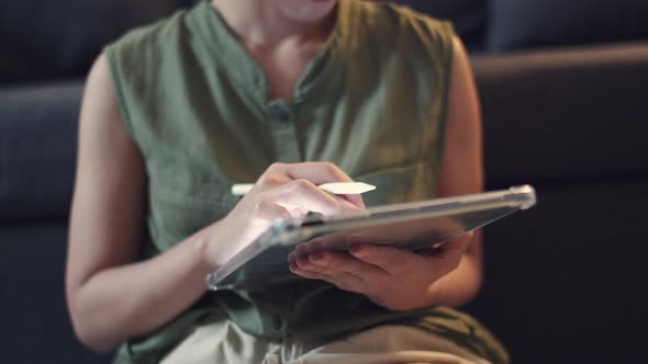 Woman hand uses a pencil to write articles on her digital tablet.