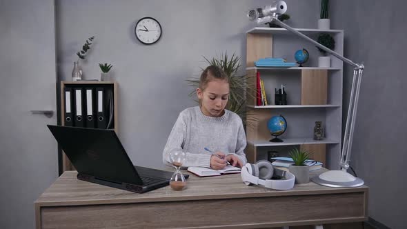  Teen Girl with Long Light Hair Sitting at Her Home Workplace and Working with Computer and Notebook alt