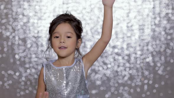 Cute Happy Little Girl Child in a Silver Dress Dancing on Background of Silver Bokeh.