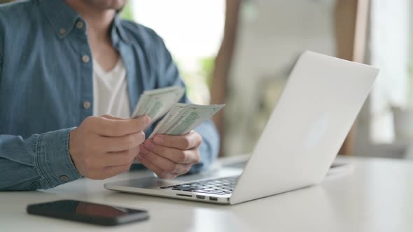 Close Up of Man Counting Dollars While Working on Laptop alt