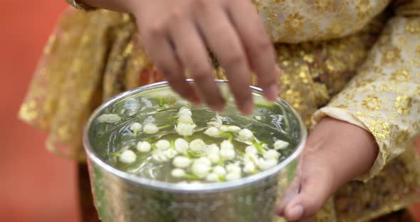 Female hand put jasmine flowers into water in bowl. alt