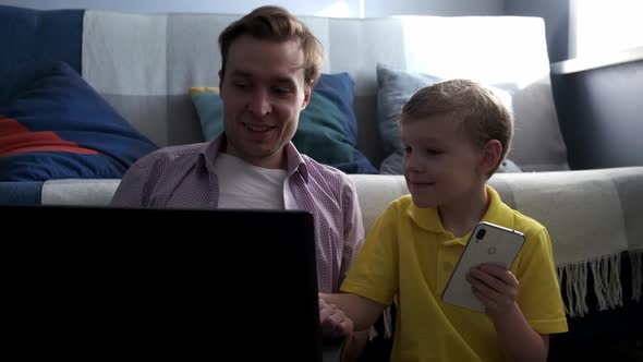 Young Dad and Little Son in Living Room Have Fun Watching Funny Videos on Laptop Smiling Father and