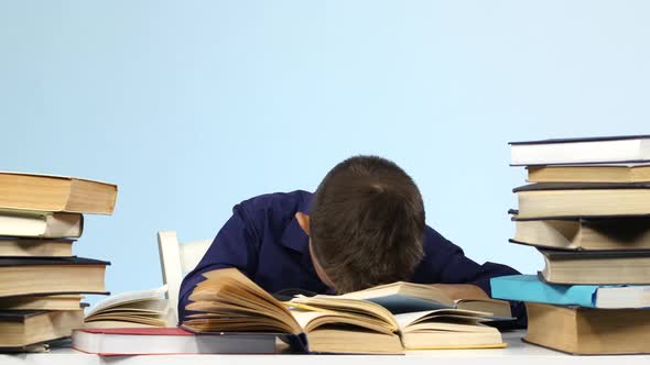 Boy Sits at the Table and Falls Asleep for a Book. Blue Background alt