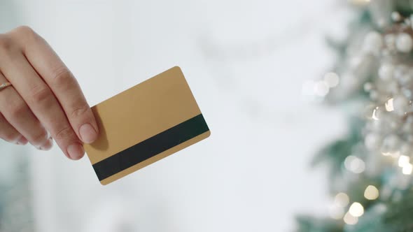 Close Up Woman Fingers Holding Plastic Card with News Year Tree on Background. alt