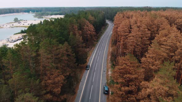 A Drone Flies Over a Road in a Forest with Parked Cars on the Side of the Road alt
