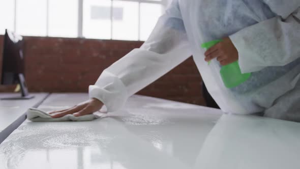 Midsection of cleaner wearing protective overalls disinfecting office and furniture alt