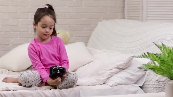 Little Child Girl Sets the Alarm in Bed