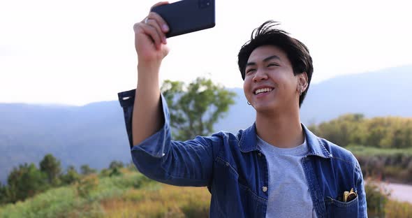 Young Asian traveler taking video with smart phone on top of the mountain. alt