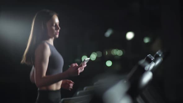 Female Athlete Run on a Treadmill and Uses a Smartphone To Communicate Aerobic Exercise and alt
