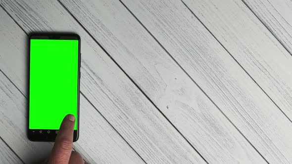 top view of a man runs his finger on a green screen of a mobile phone. Mobile app mockup.