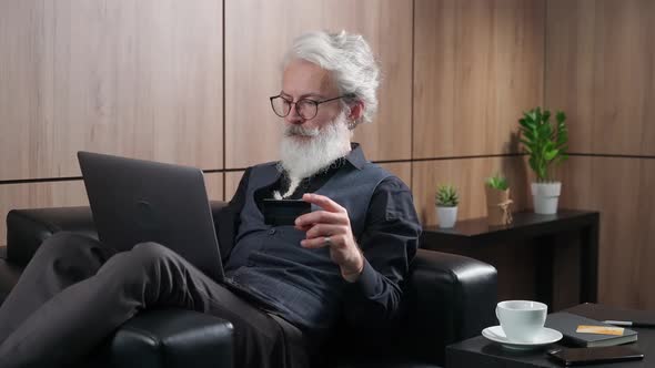 Elegant Grayhaired Man Makes Successful Purchases Online Using a Laptop and a Credit Card Adult Man alt