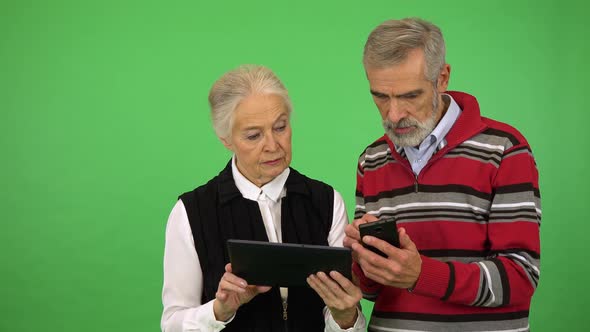 An Elderly Couple Works on a Smartphone and a Tablet - Green Screen Studio alt