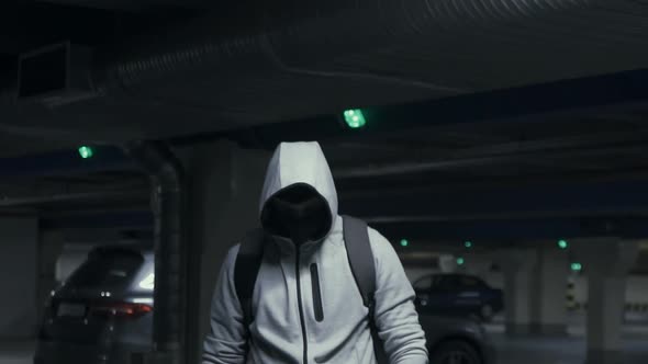 Man Criminal in the Balaclava and Hood Looking at the Camera in Underground Parkingslow Mo alt