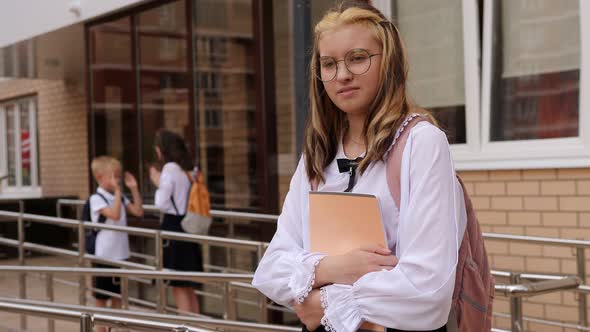 A Teenage Girl with Notebooks in the School Yard Near the Entrance to the School alt