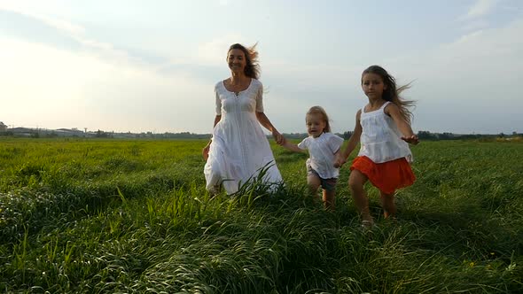 Young Mom Walks and Runs With her Little Daughters, Children on Green Grass alt