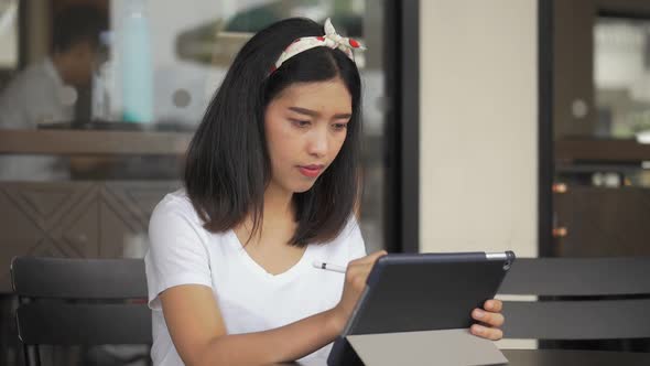 Asian businesswoman creative designer using a tablet in coffee shop.