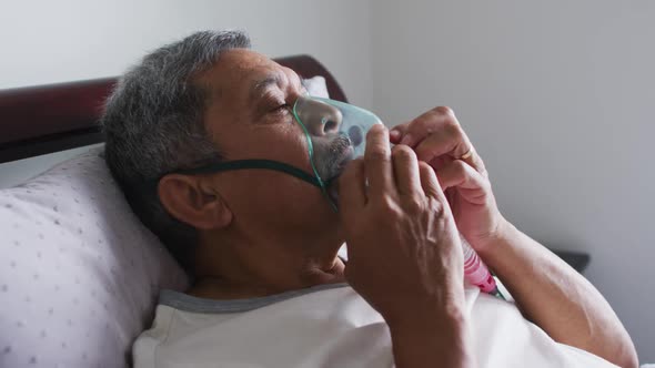 Senior mixed race man lying in bed at home using a face mask ventilator alt